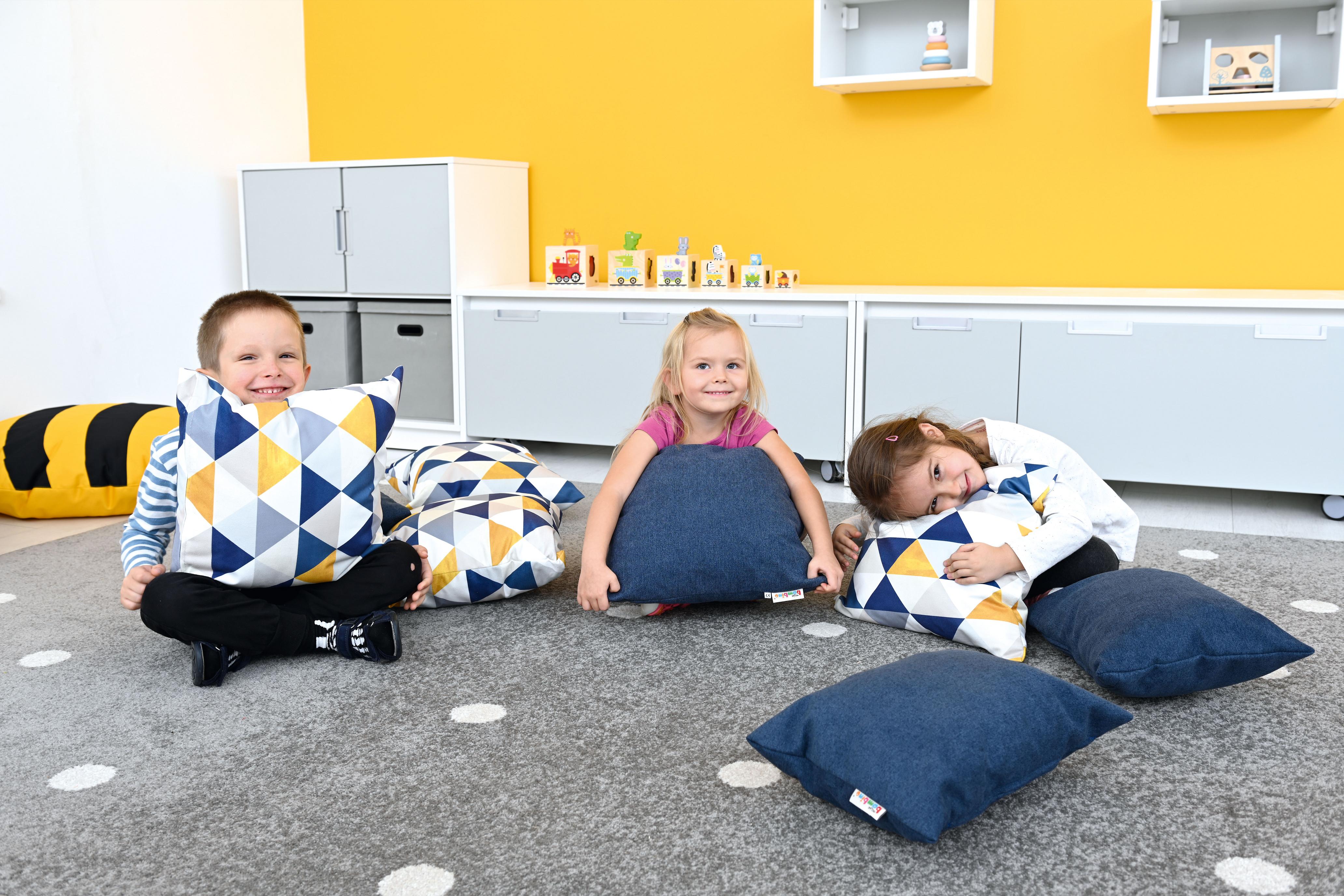 Kinder spielen mit Kissen für Sitzlandschaft im Gruppenraum.