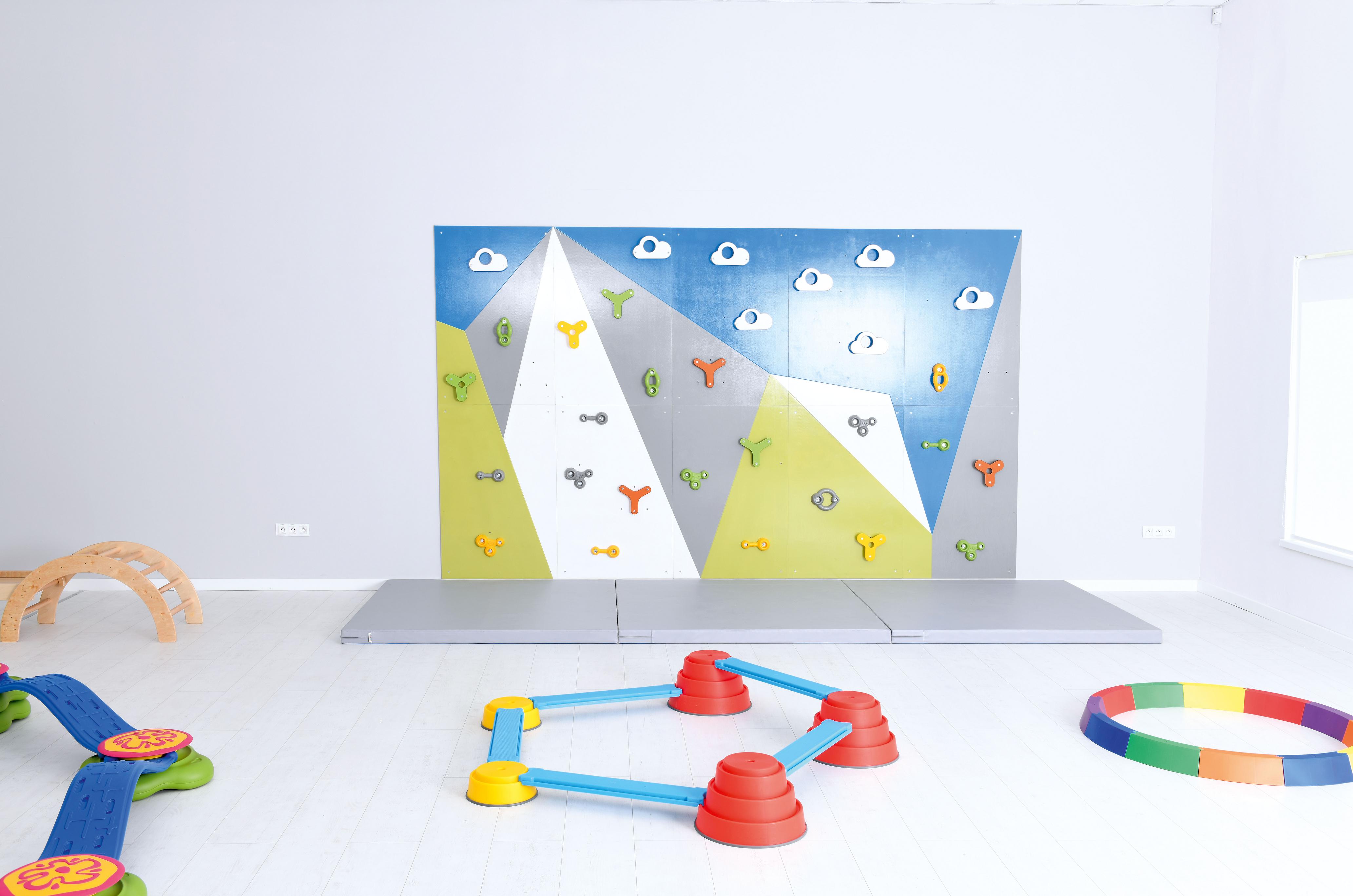 Bunte Kletterwand mit Sicherheitsmatten und Spielgeräten.