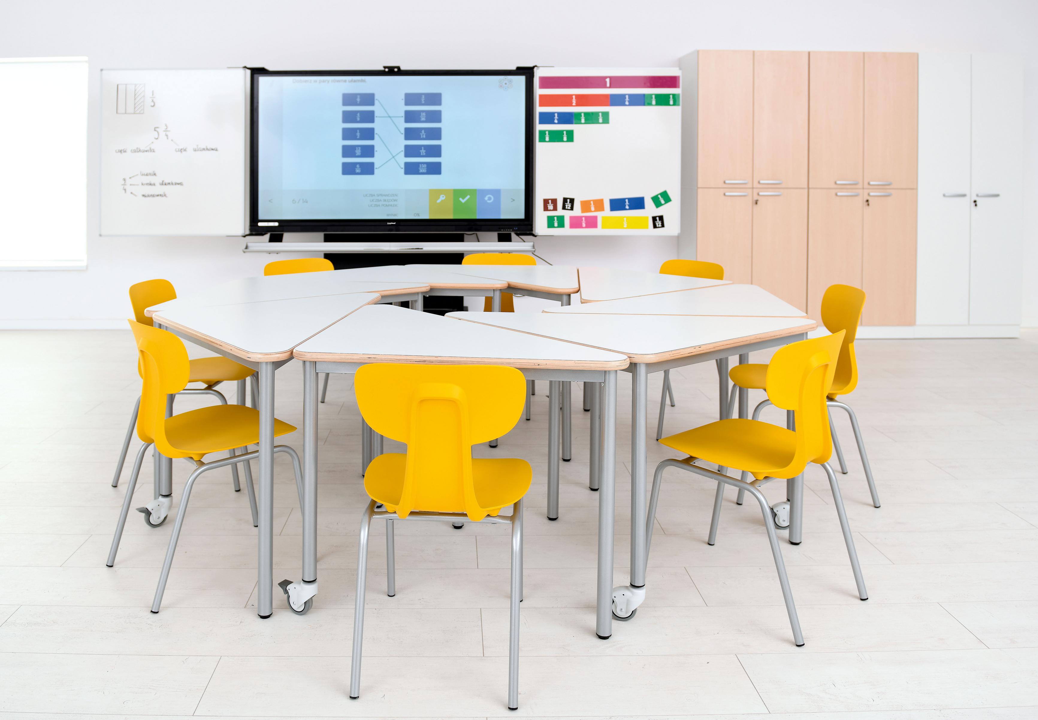 Gelbe Schülerstühle um Tische im Klassenzimmer angeordnet.