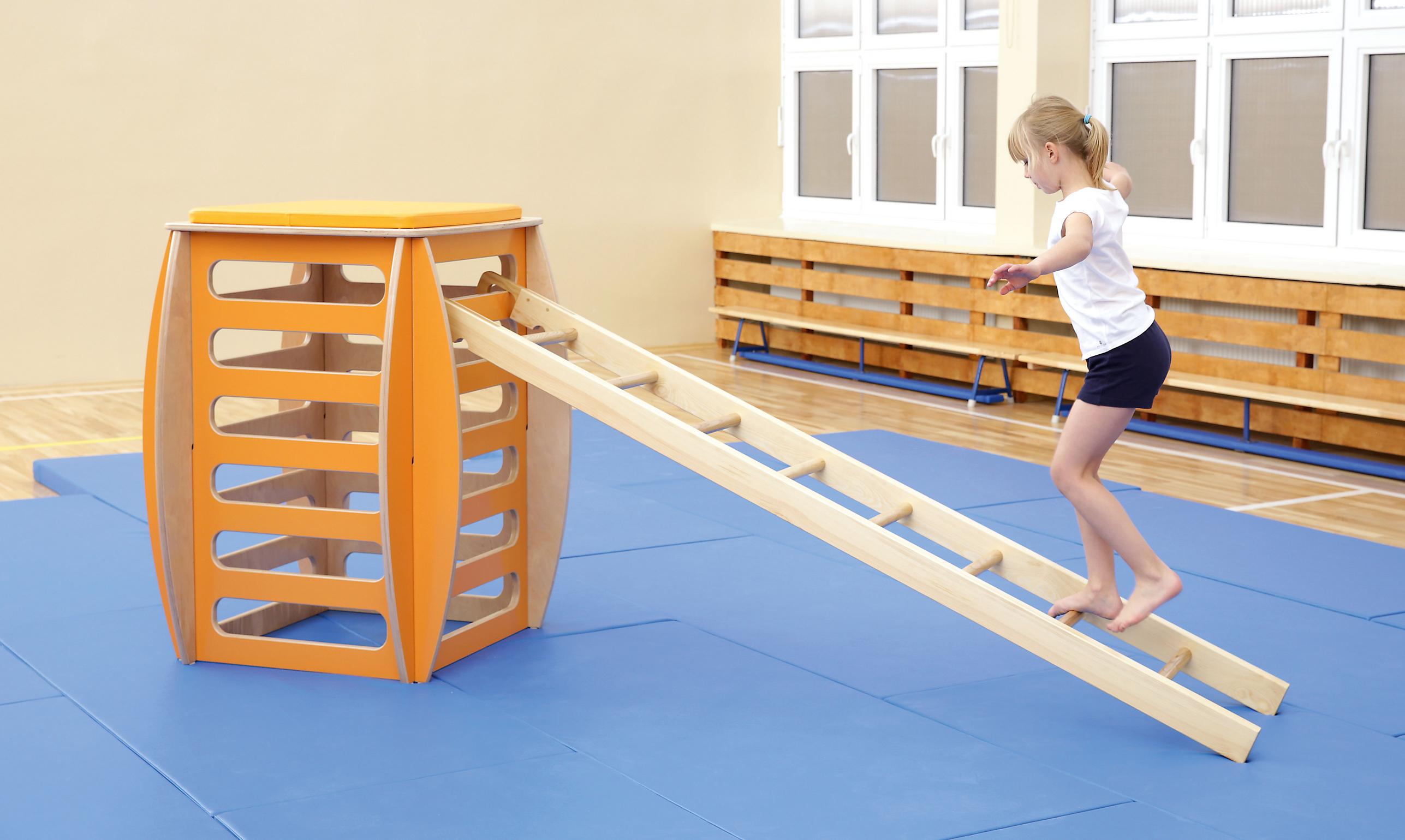 Kind balanciert auf Turnpodest in Schulturnhalle.