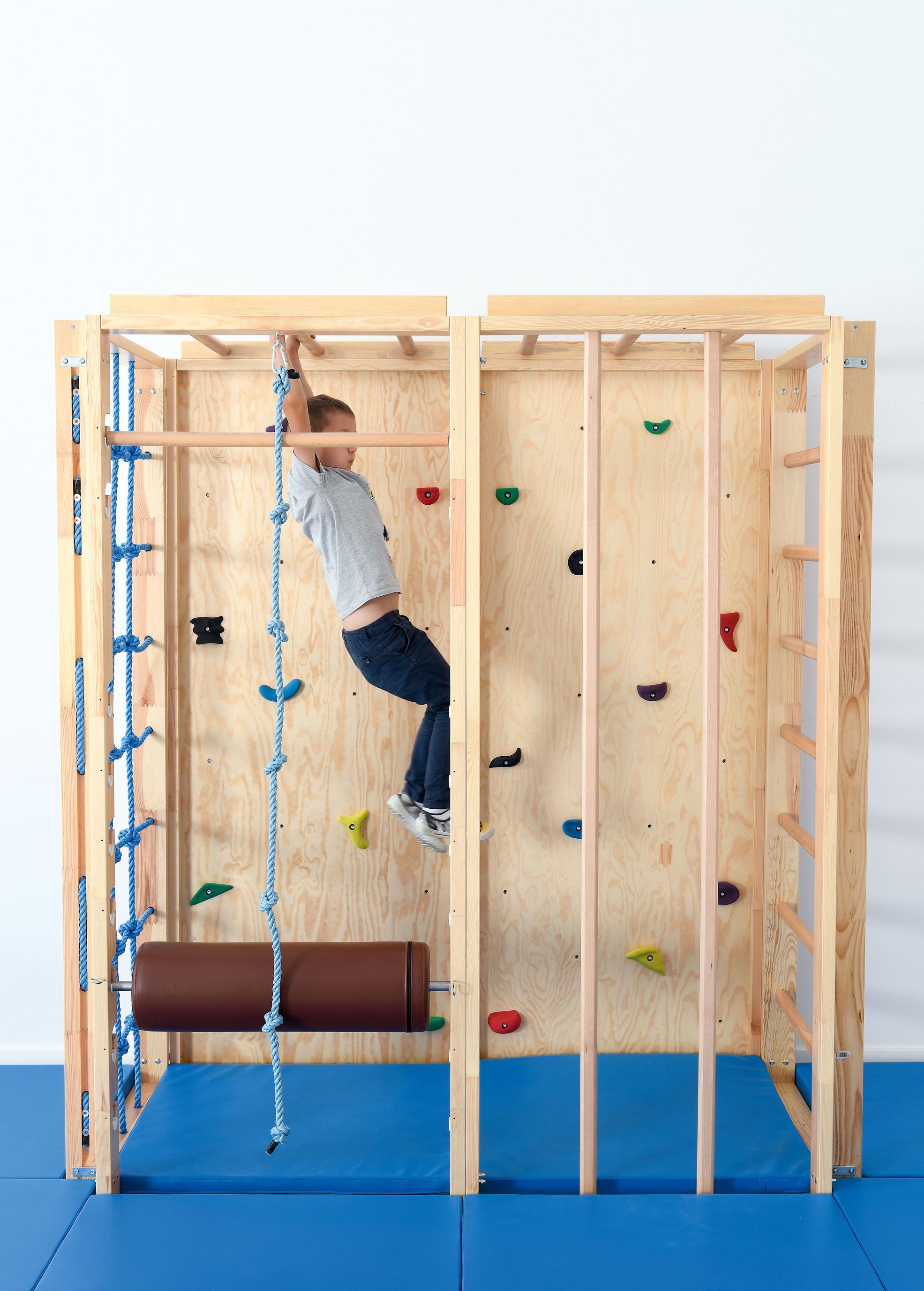 Kind klettert an der Turnhallen-Kletterwand mit Seil.