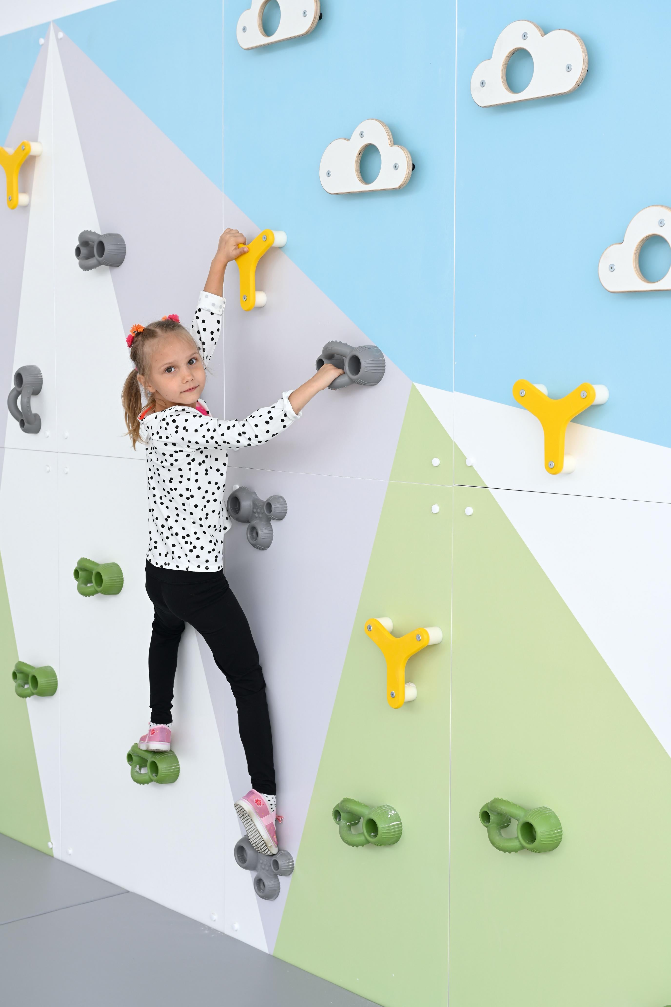 Kind klettert auf bunter Kletterwand in Sporthalle.