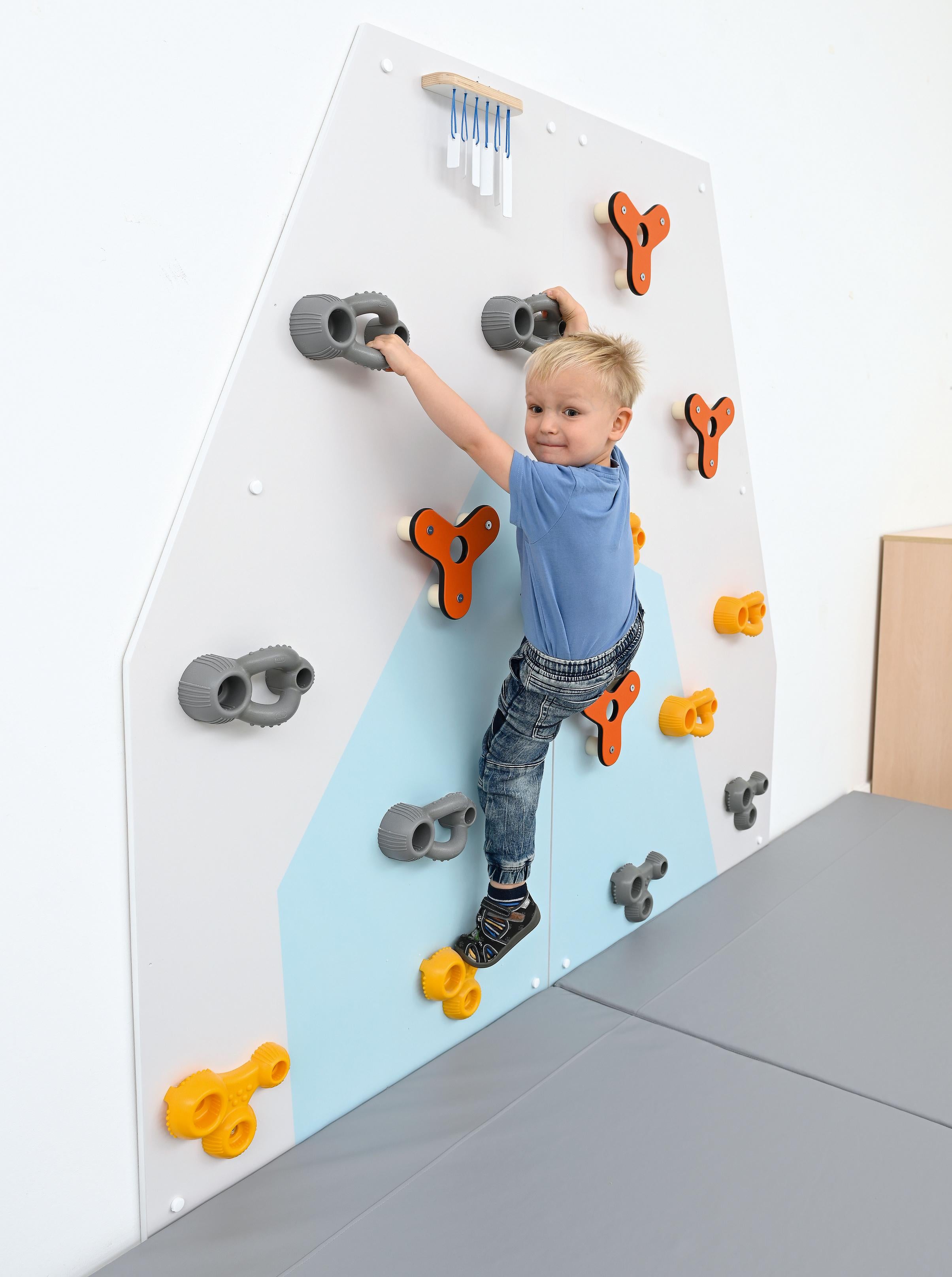 Kind klettert freudig an bunter Kletterwand für Kita.