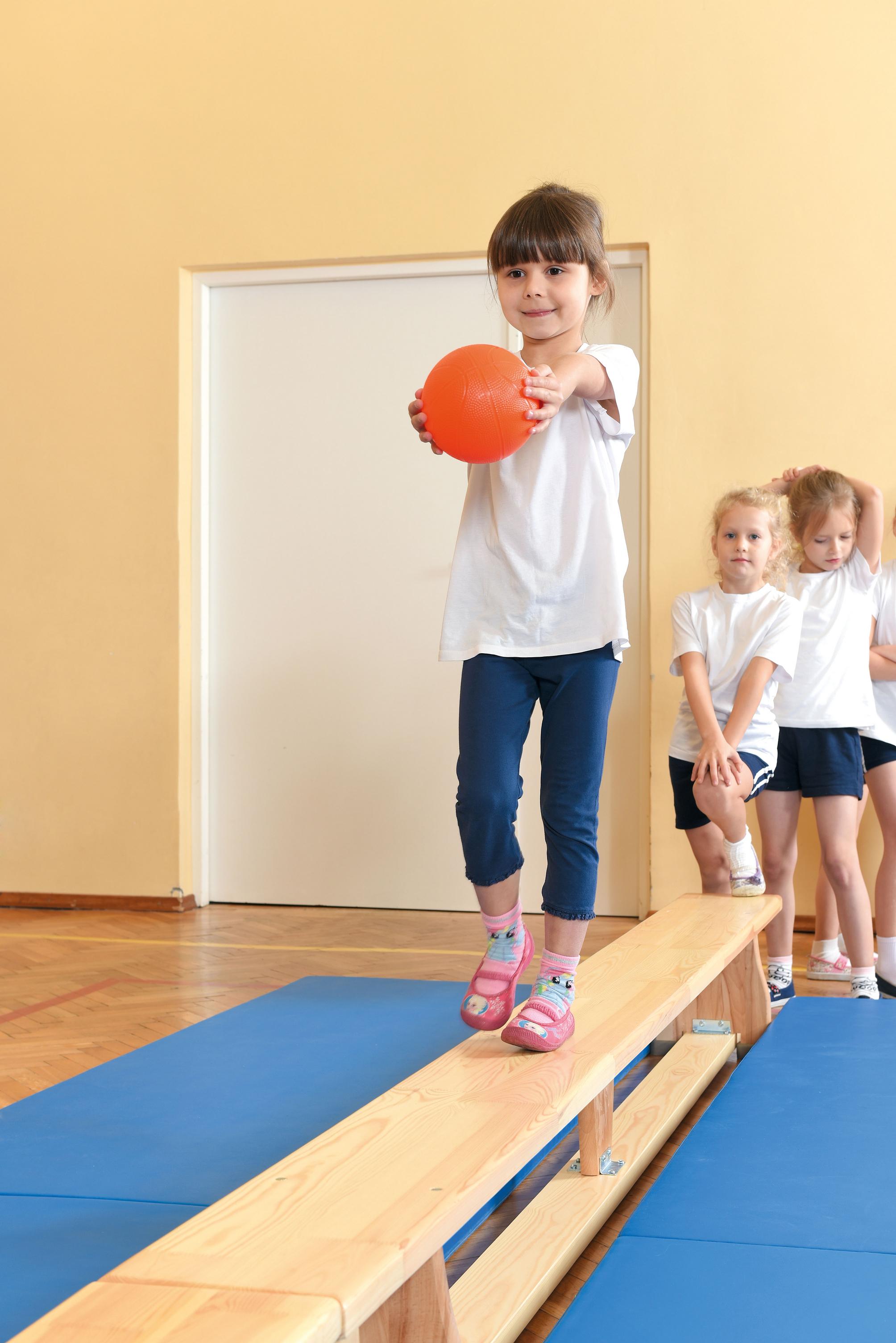 Kinder balancieren auf Turnbank 3 m im Bewegungsraum.