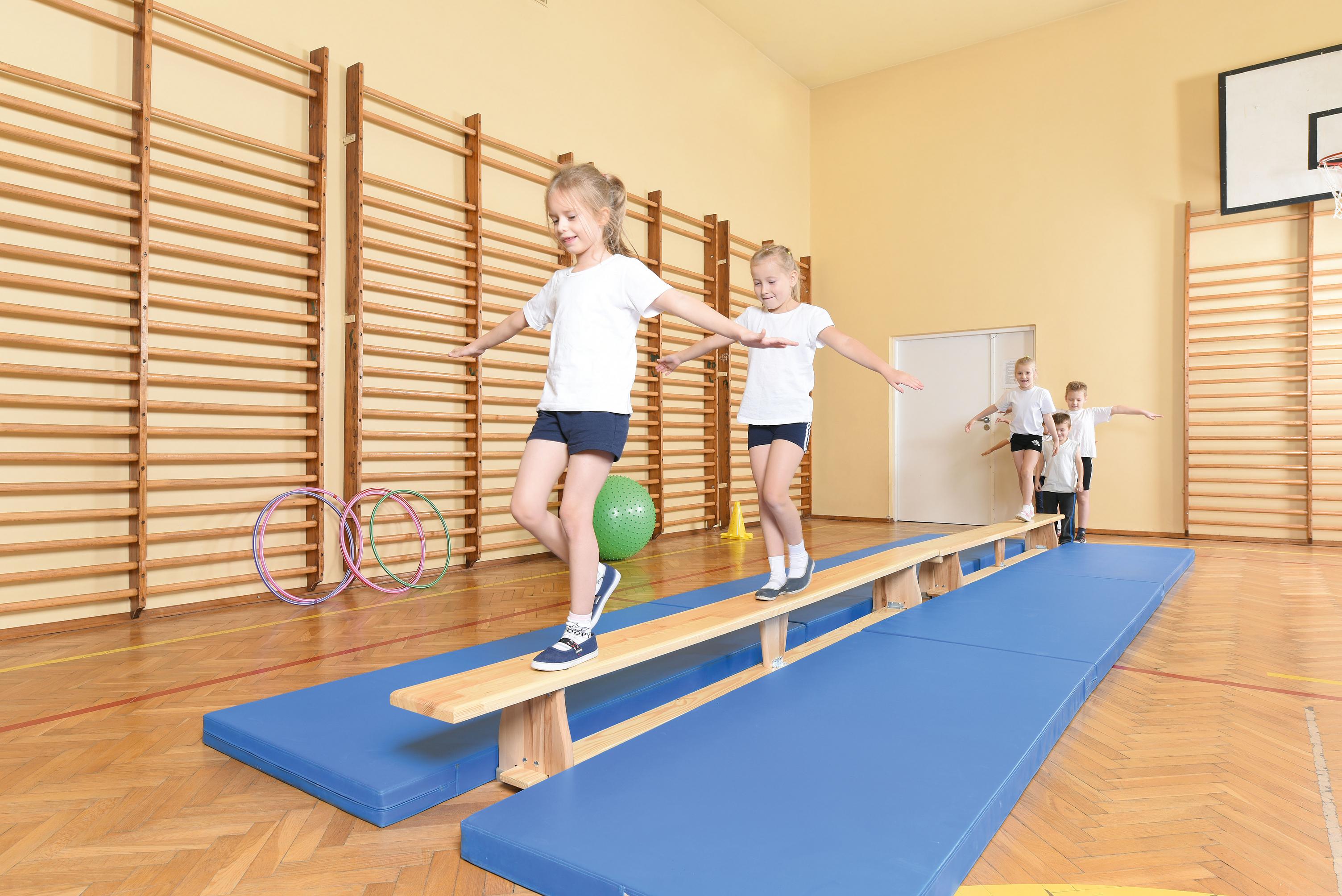 Kinder balancieren auf Turnbank 3 m im Sportraum.