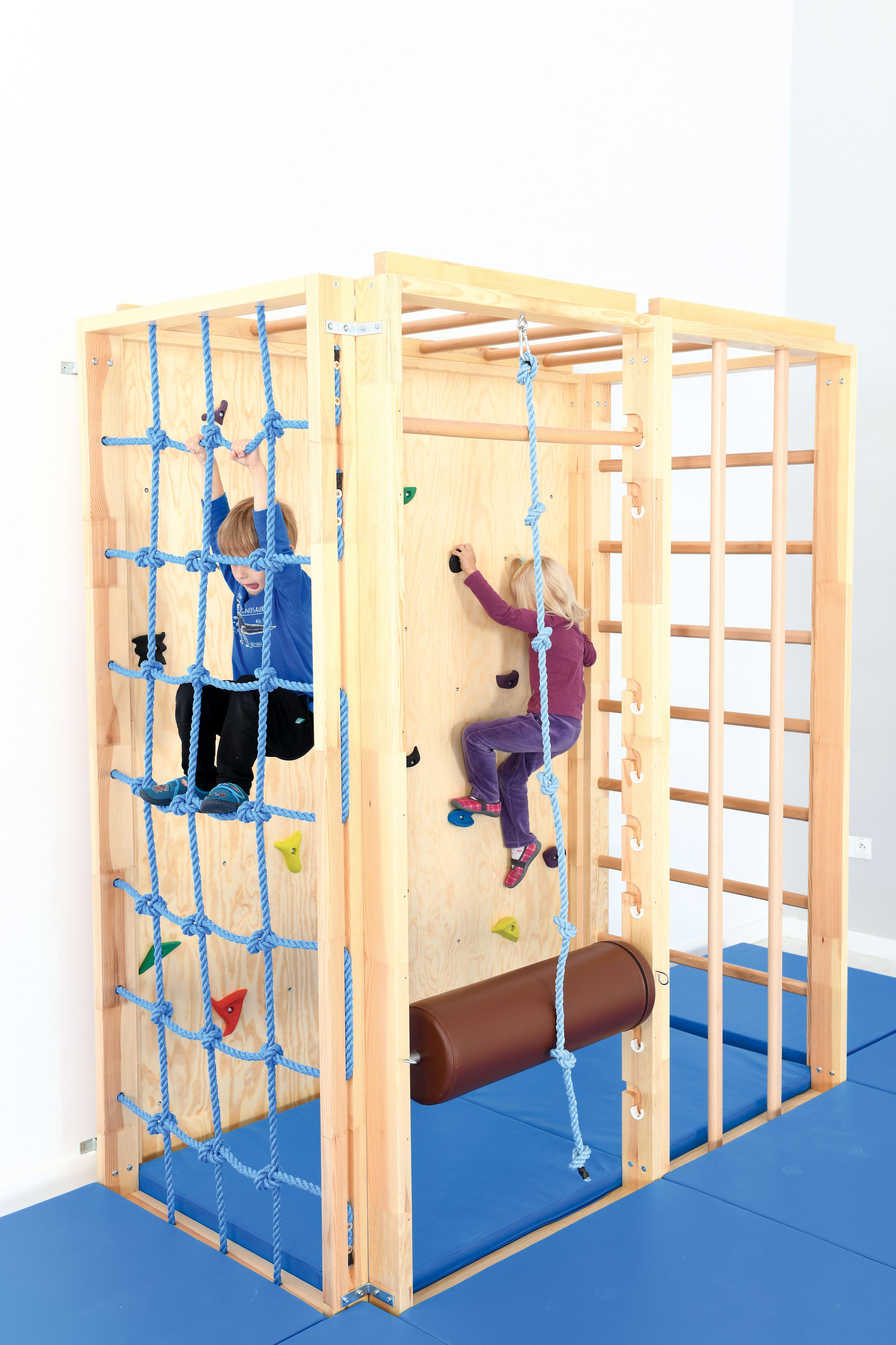 Kinder klettern an bunter Kletterwand in Turnhalle.