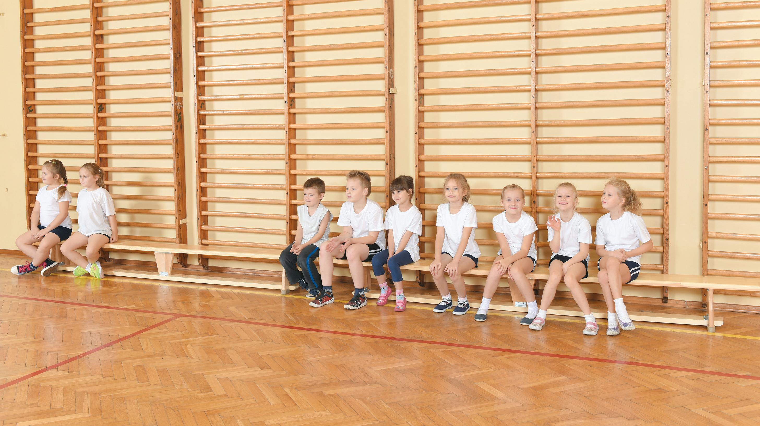 Kinder sitzen auf Turnbank 3 m im Turnraum.