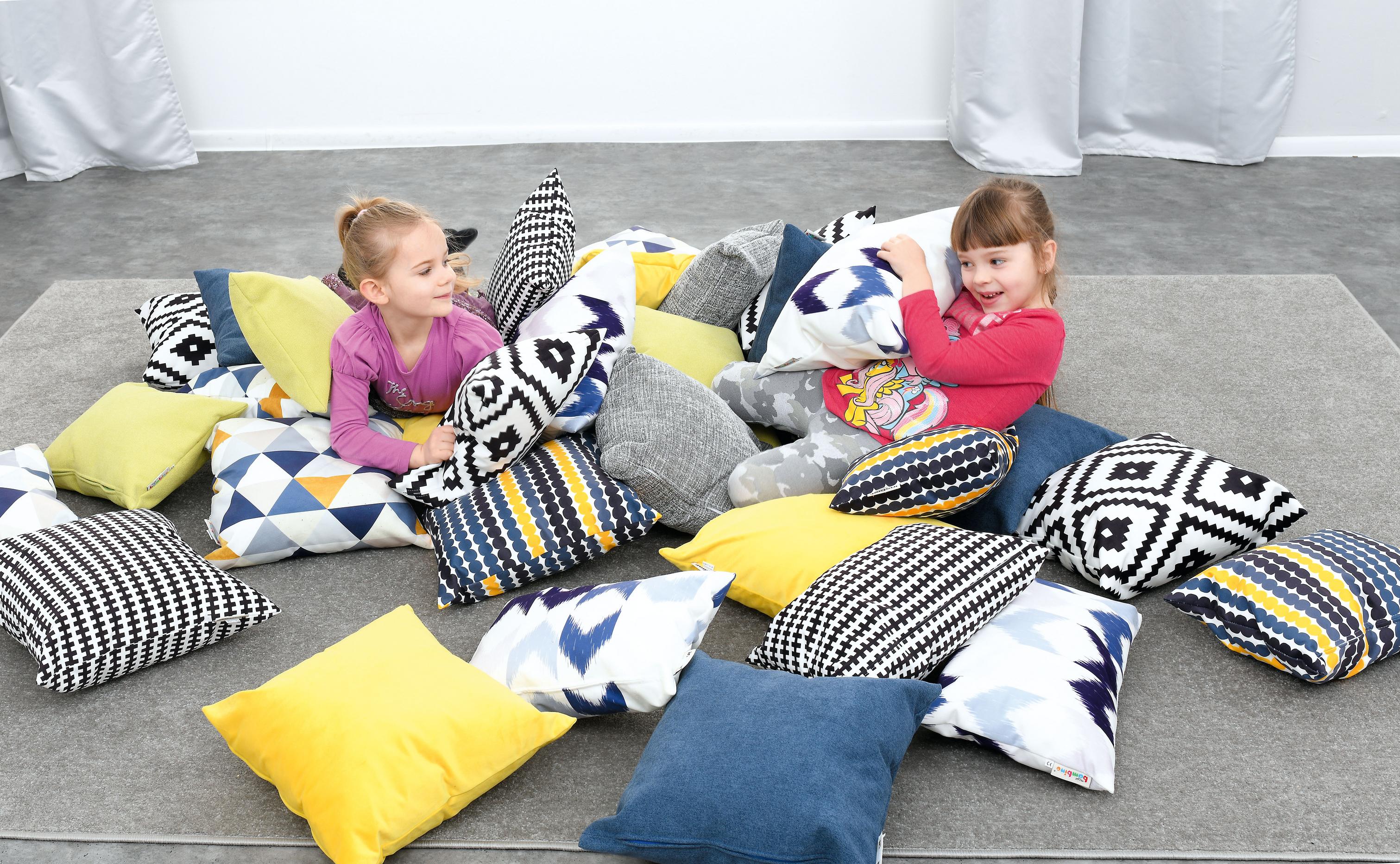 Kinder spielen auf bunten Kissen für Sitzlandschaft.