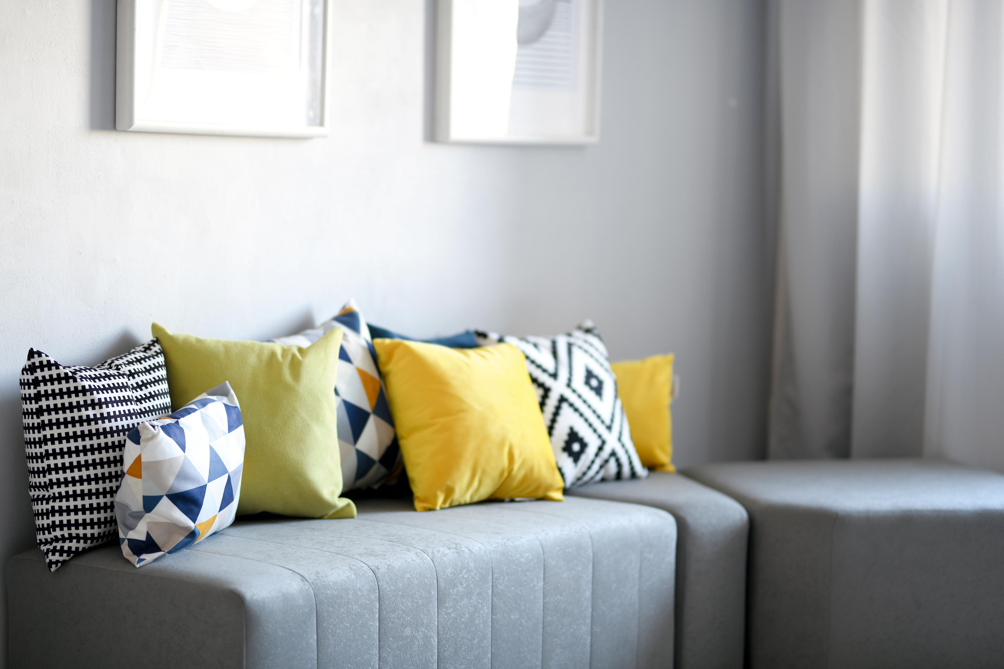 Bunte Kissen auf grauer Sitzlandschaft im Raum.